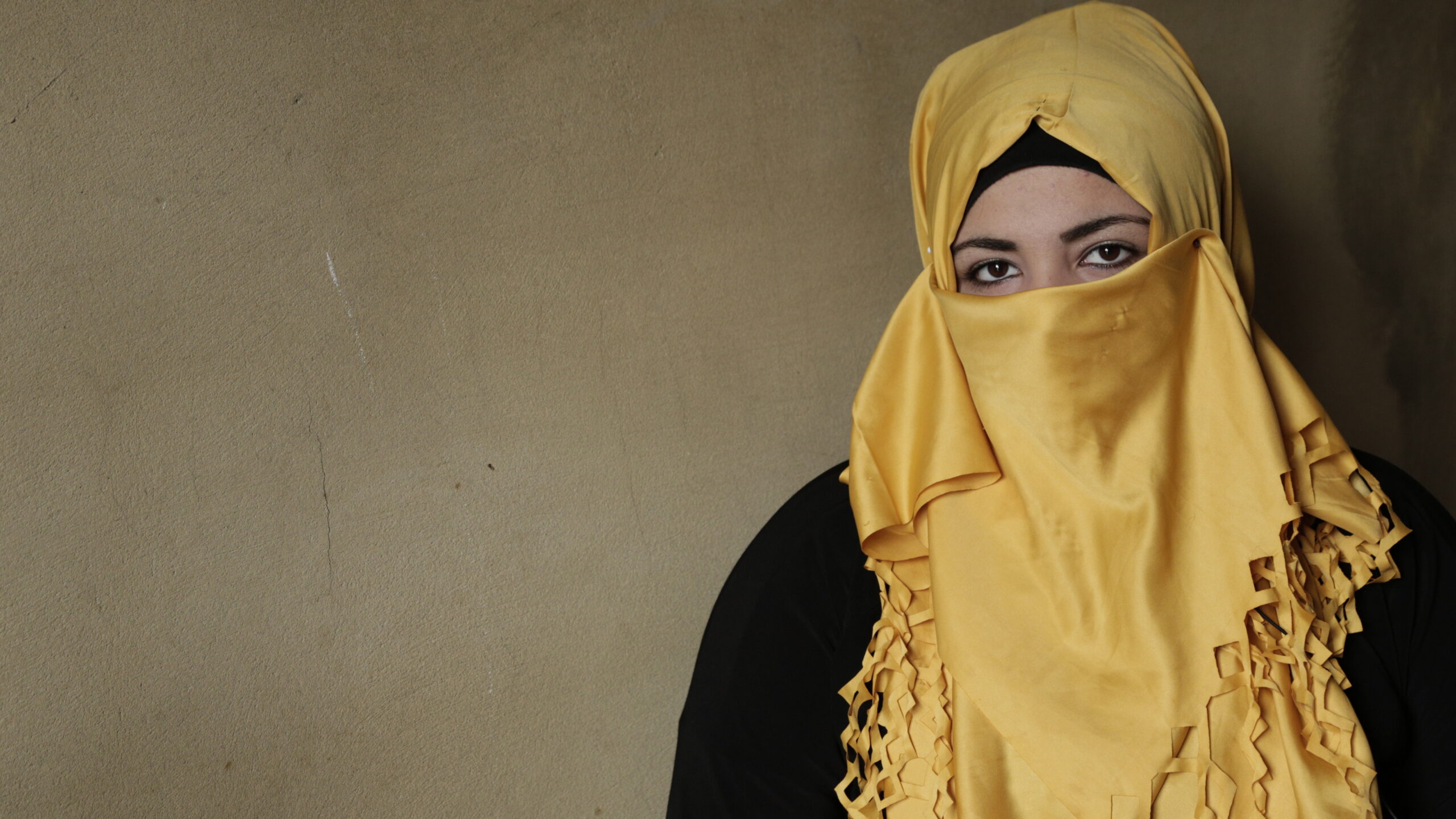 A girl in a yellow niqab looks at the camera.