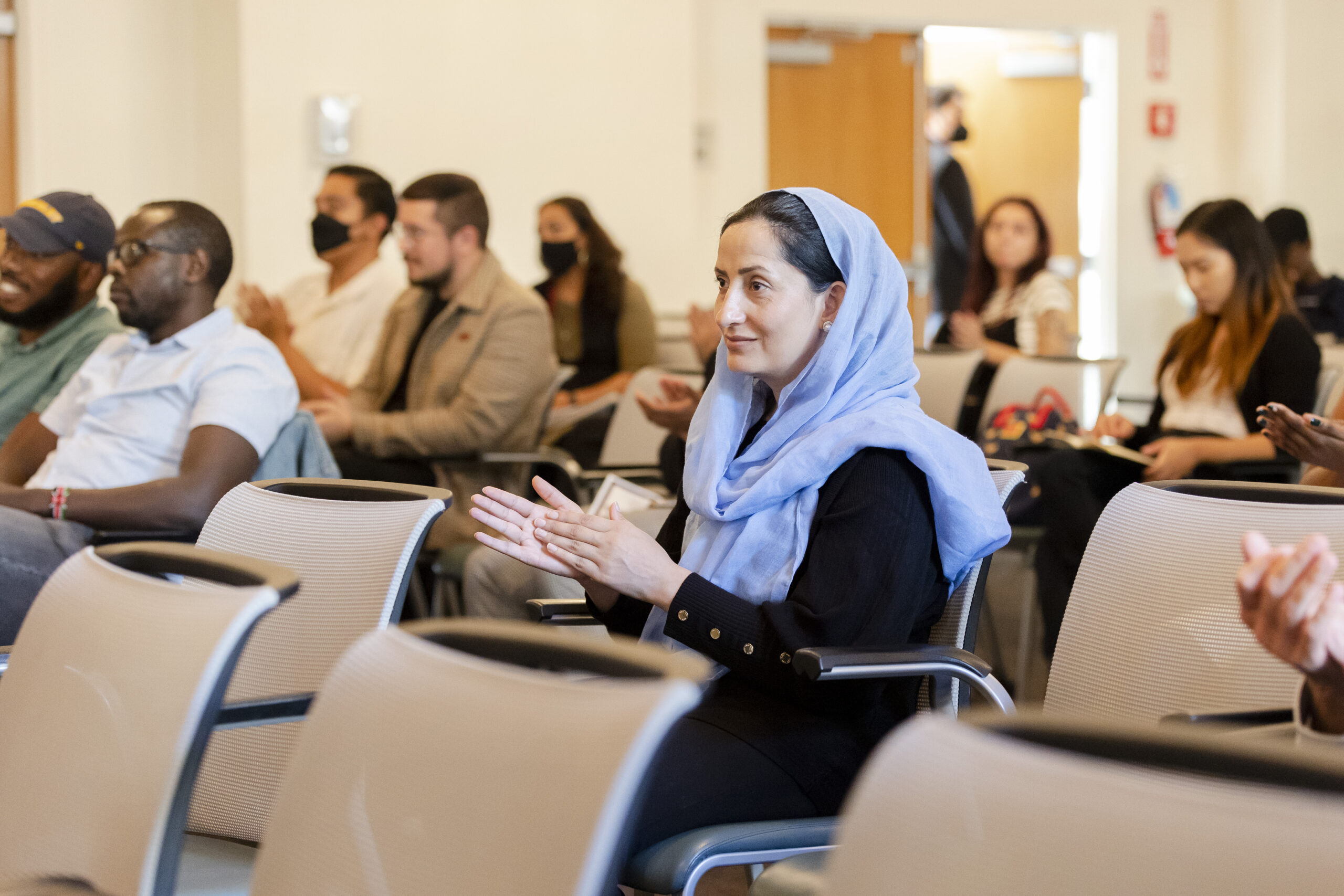 A woman wearing a blue hijab claps at an event.