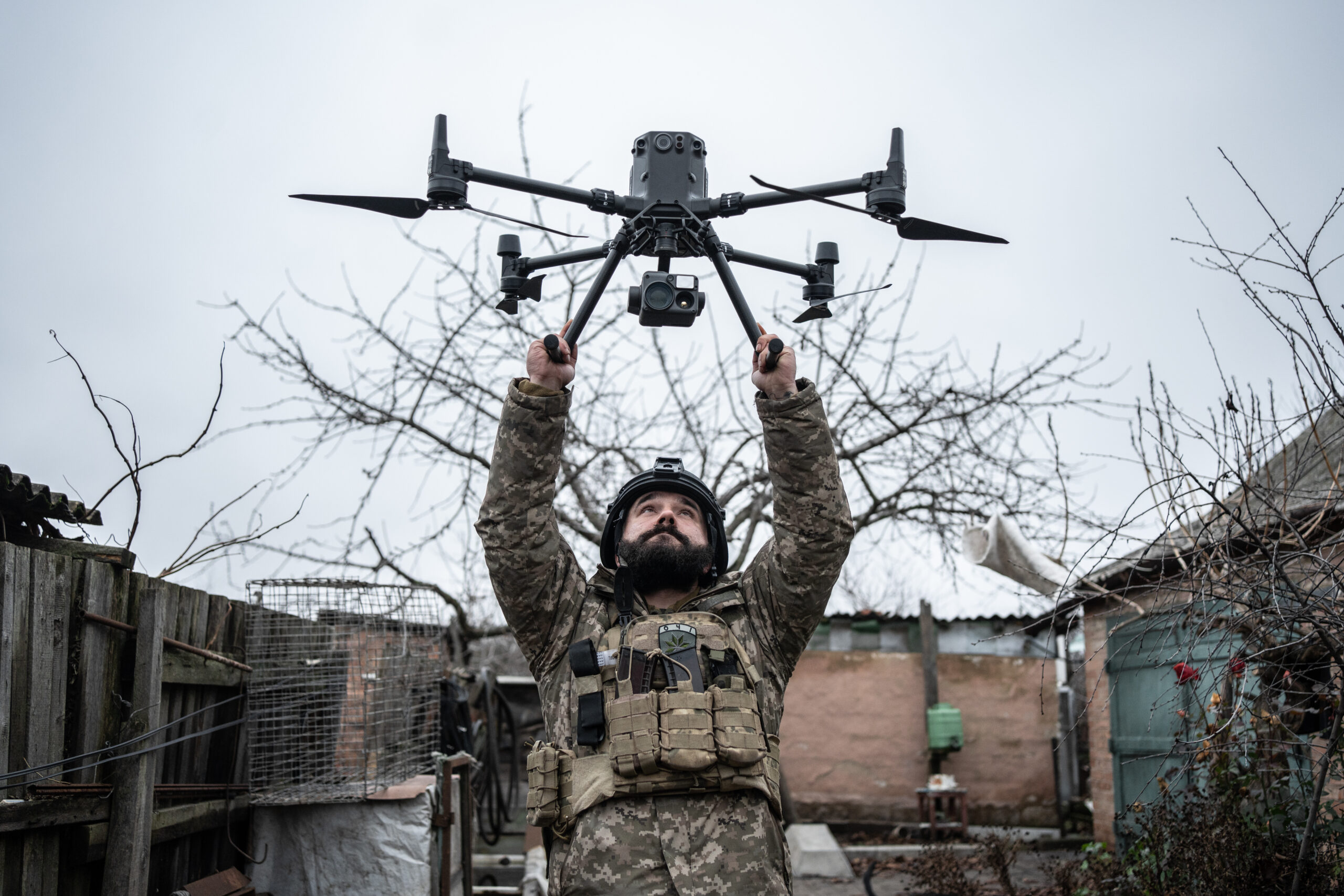 A male soldier holds a drone in the air.
