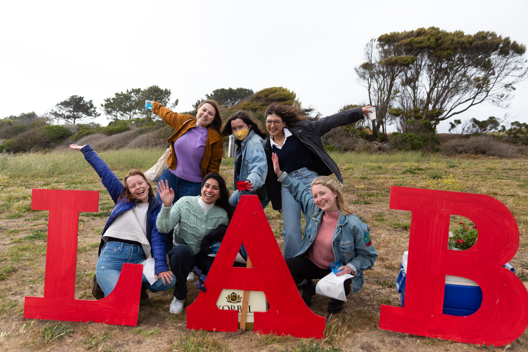 Students cheer while posing outside with giant red letters spelling 