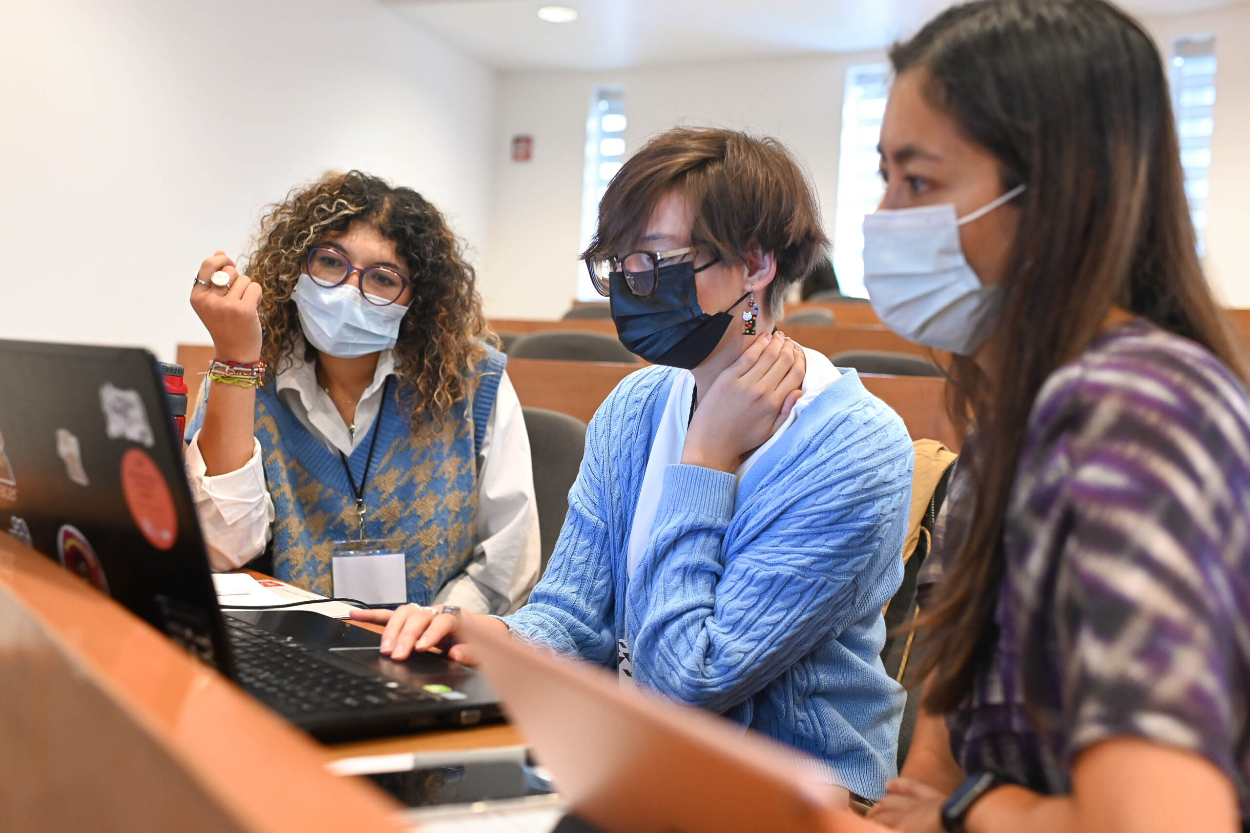 Three masked individuals work on a single computer.