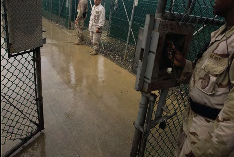 Several men in U.S. army uniforms walk inside a gated area.