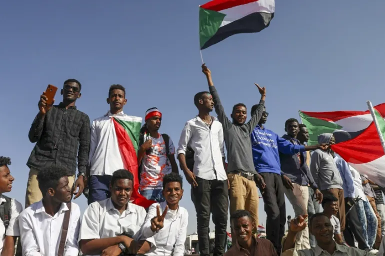 A group of people wave multiple Sudanese flags.