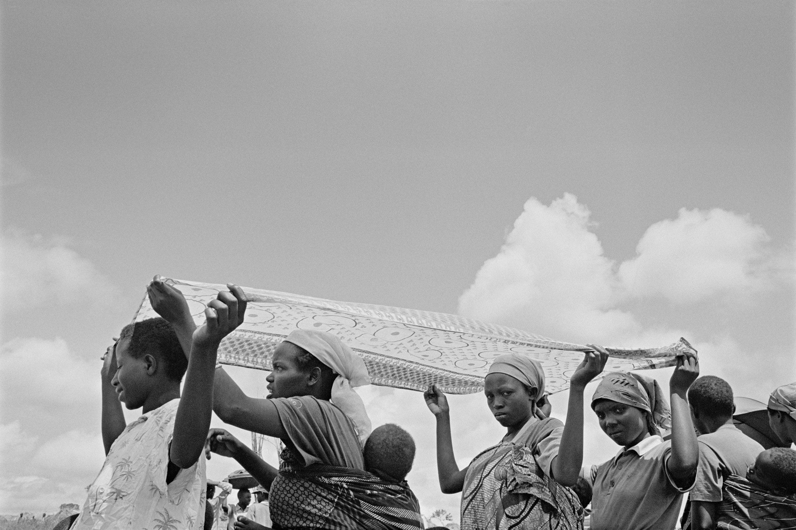 Women and children walk, holding a blanket to shield from the sun.