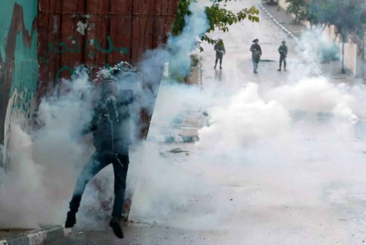 A protester attempts to throw a canister back at Israeli soldiers during clashes at Aida refugee camp (AFP)