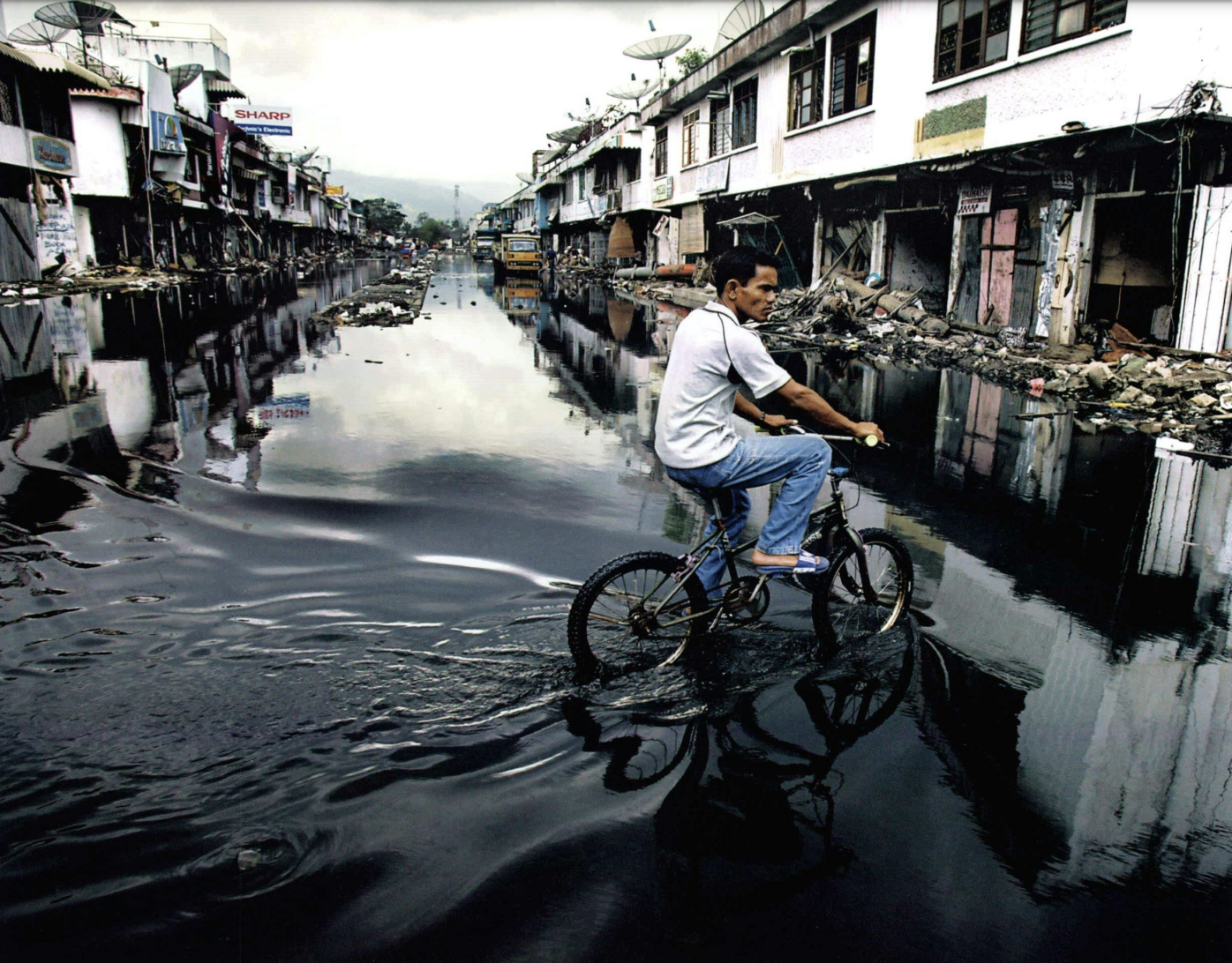A man rides a bike through a flooded street.