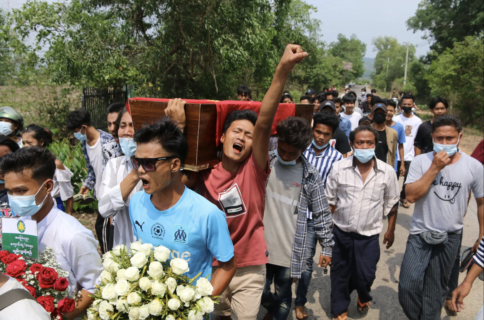 A funeral procession depicts a group of people carrying a coffin. One man has his fist in the air. People are crying.