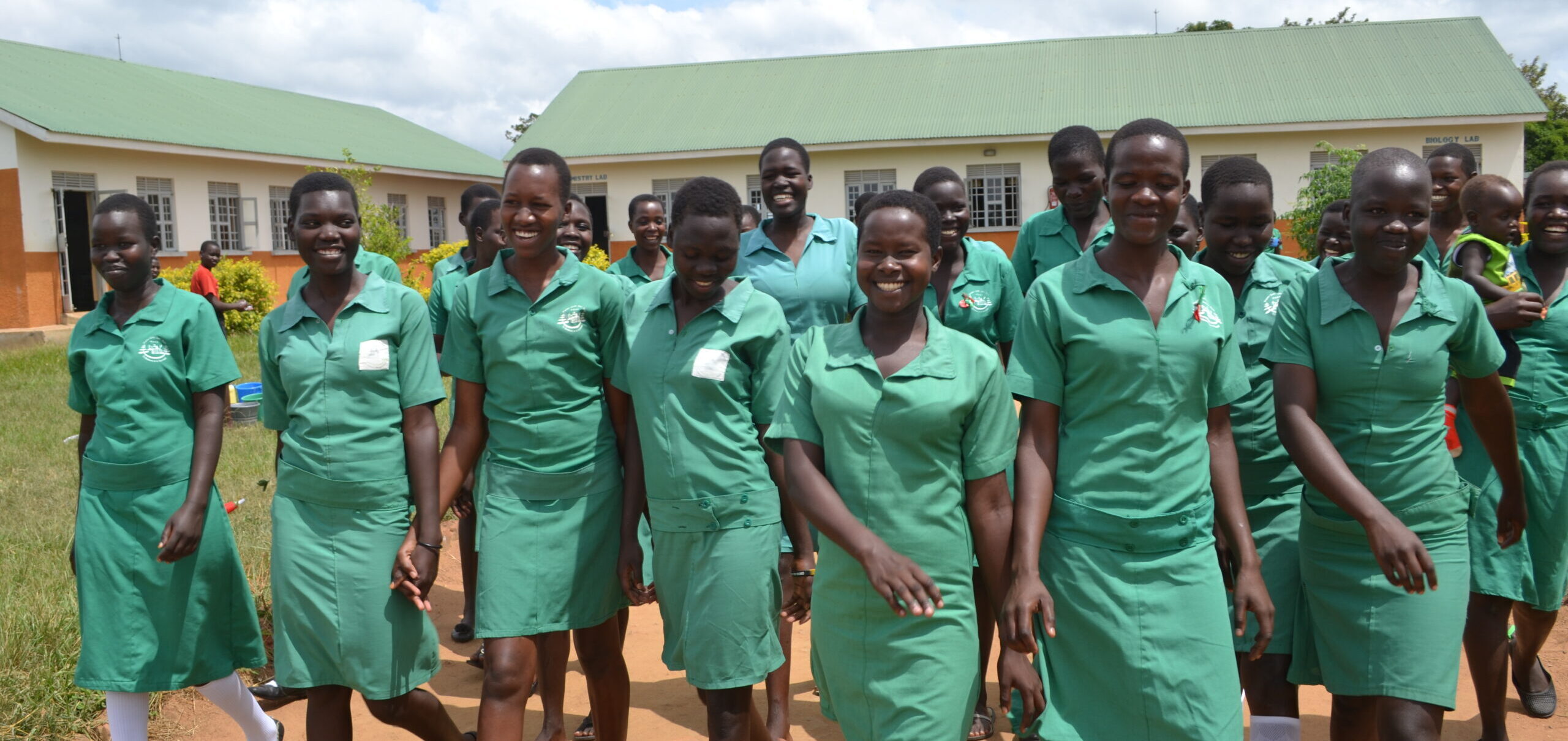 Girls smile and walk together, all wear green uniforms.