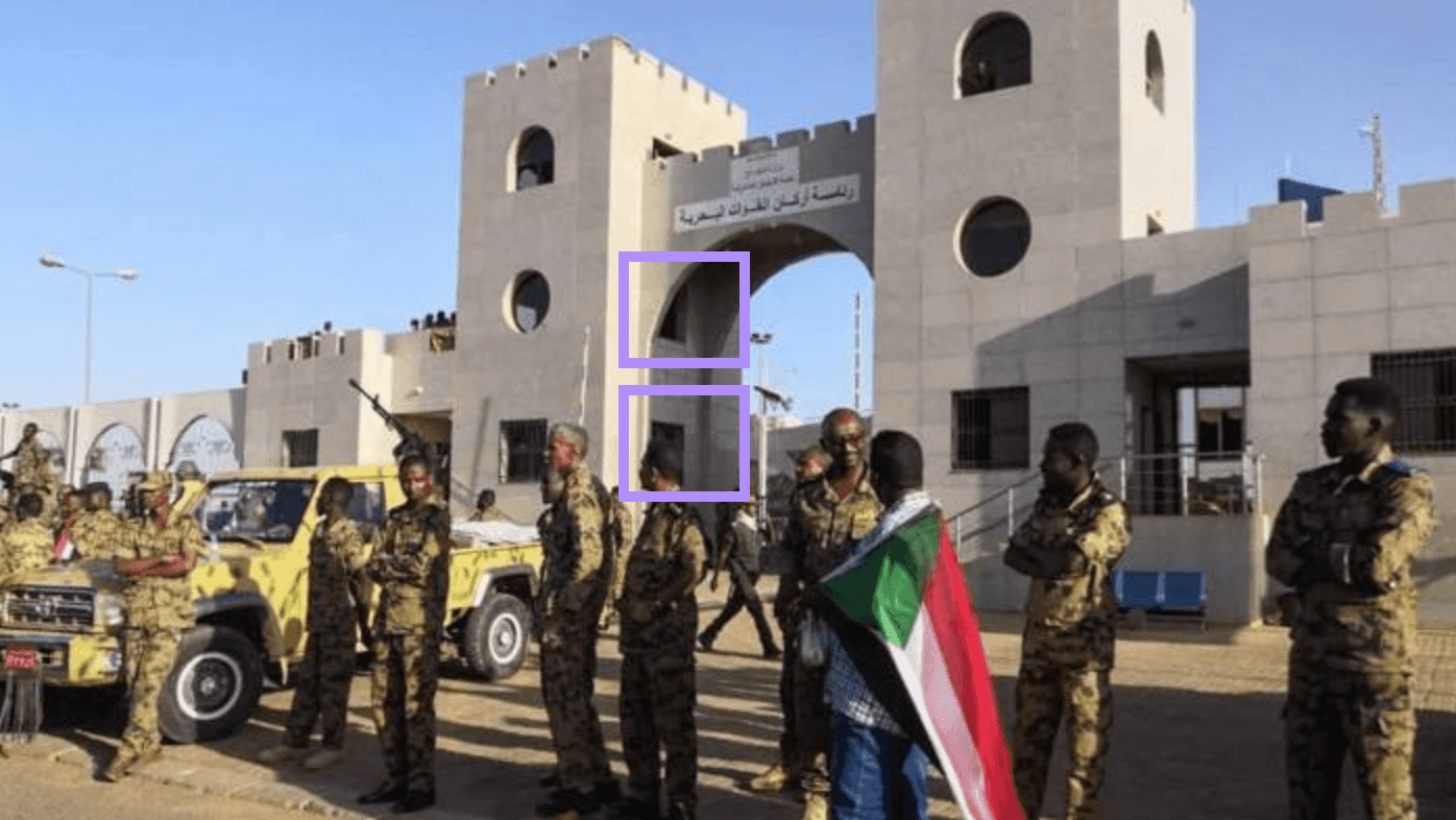 Soldiers stand outside a building with a high archway. One person holds the Sudanese flag.