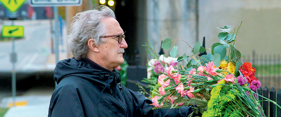 A man with glasses holds flowers.