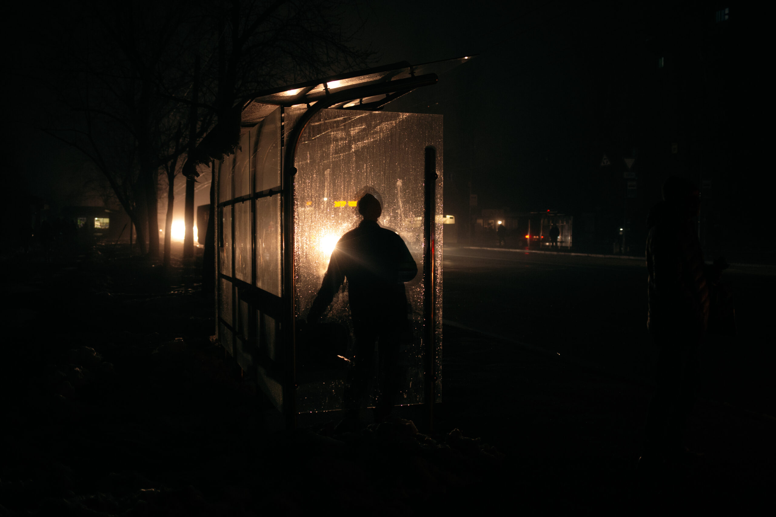 A person silhouetted against a bus stop walks into a dark night.