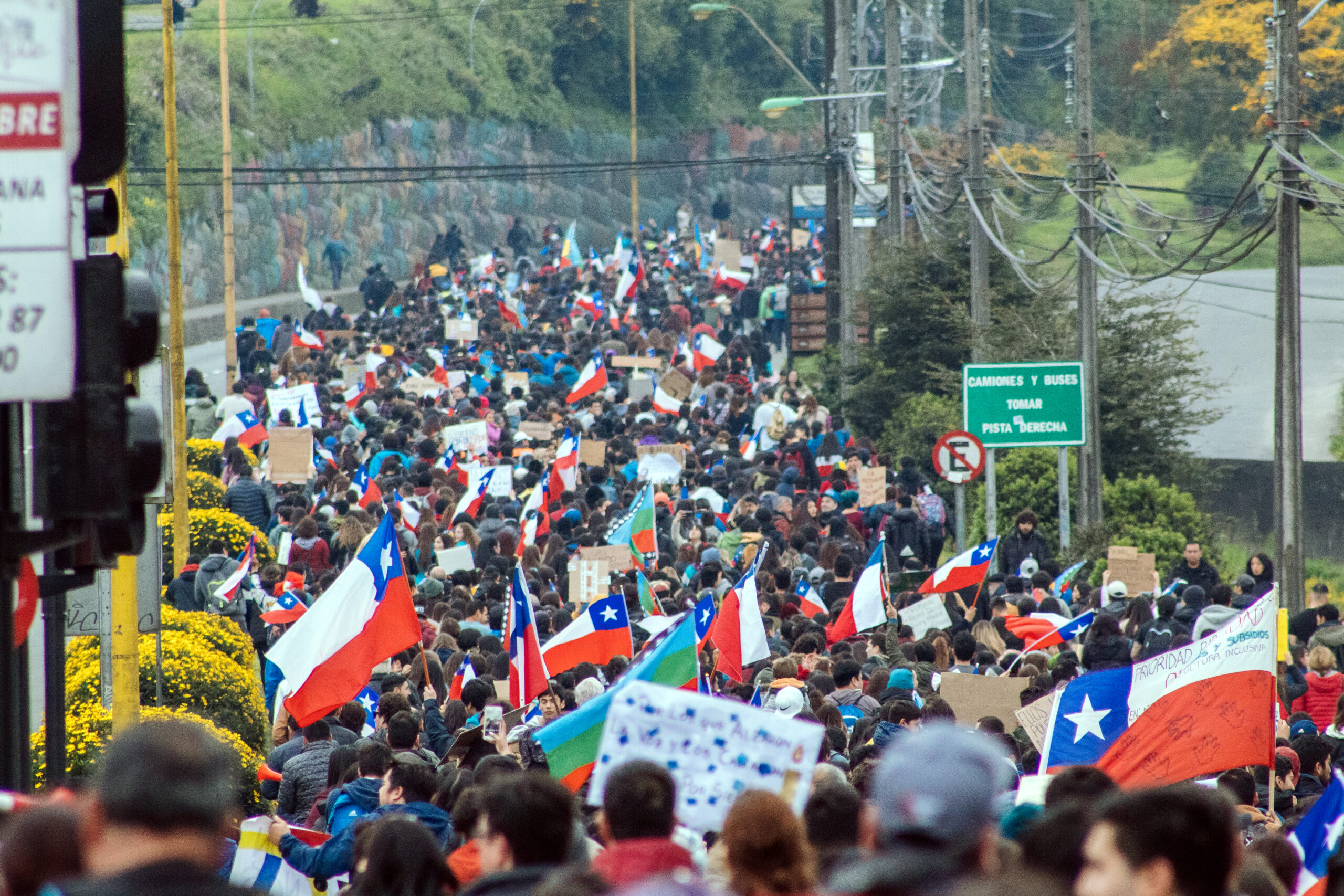 A group of people fill the street in protest. Some wavre the Chilean flag.