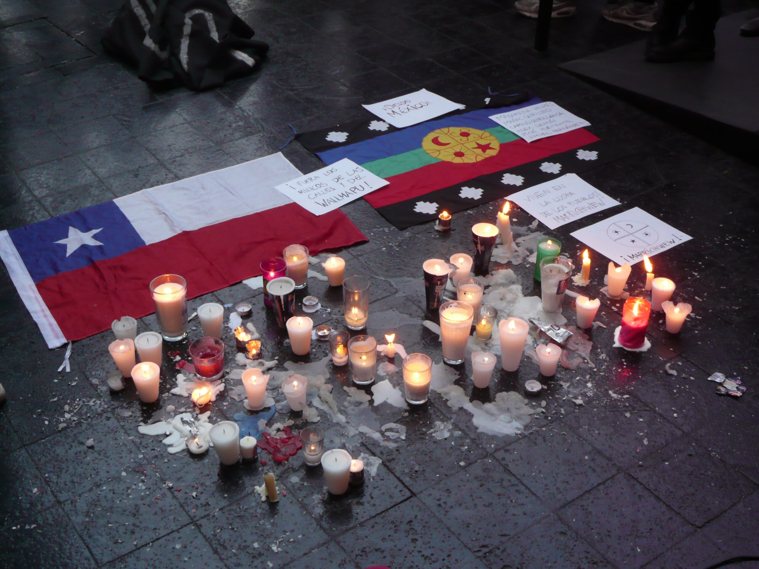 A Chilean flag is surrounded by candles and messages on the ground.