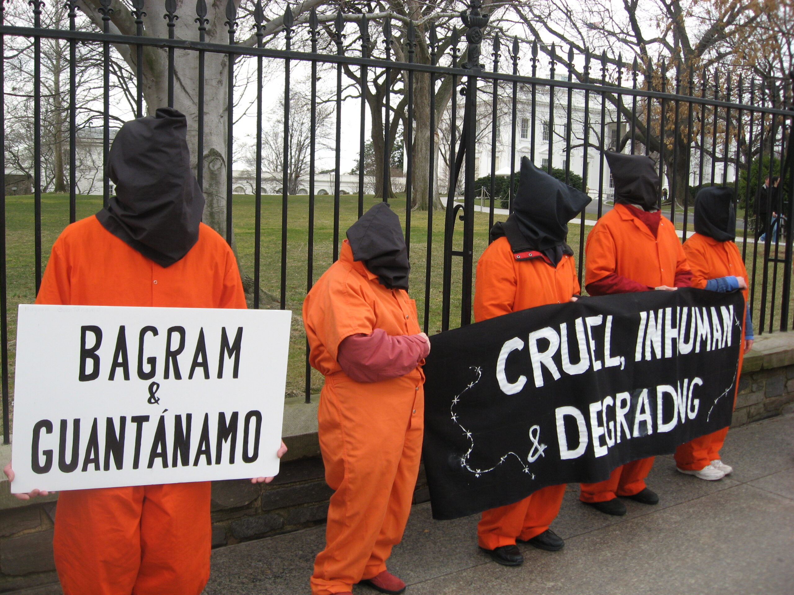 People stand in orange jumpsuits and carry signs that read 