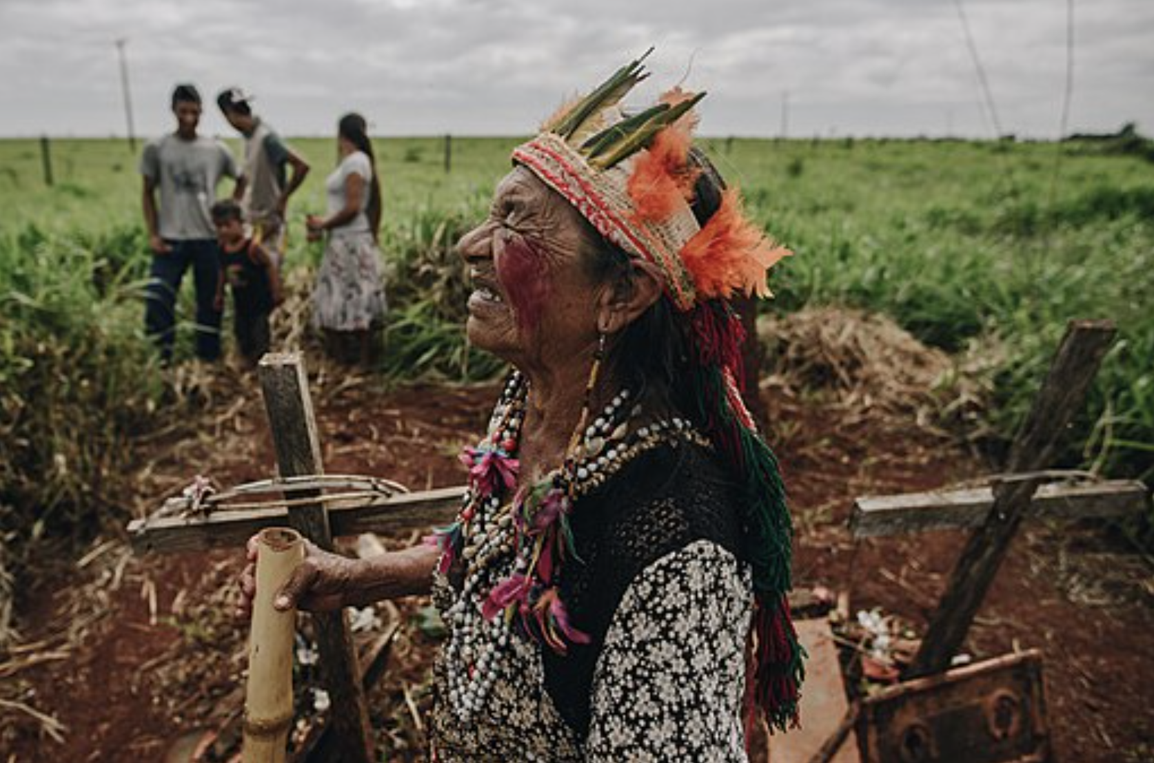 A woman cries in a cemetery. She is wearing feathers and beading.