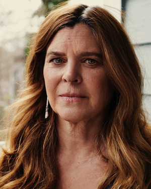 A woman with red-brown hair looks stoically into the camera.