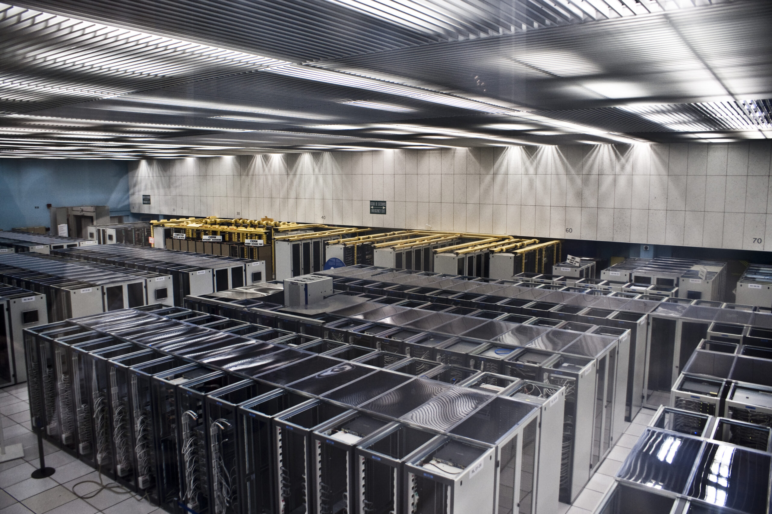 A room with data processing servers. The servers are large rectangles and are shown standing shoulder-to-shoulder with one another.