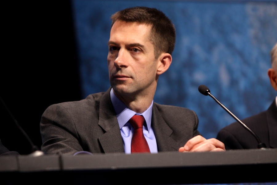 A man sits at a lectern with a microphone. He is not looking at the camera.