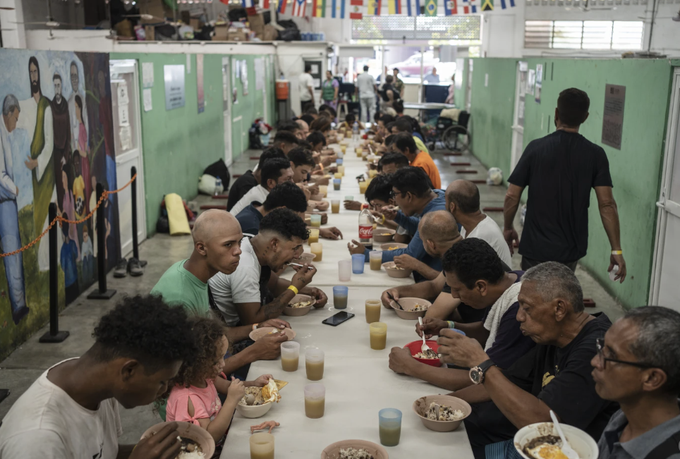 A group of people eat bowls of food at a table. None of them are looking at the camera.